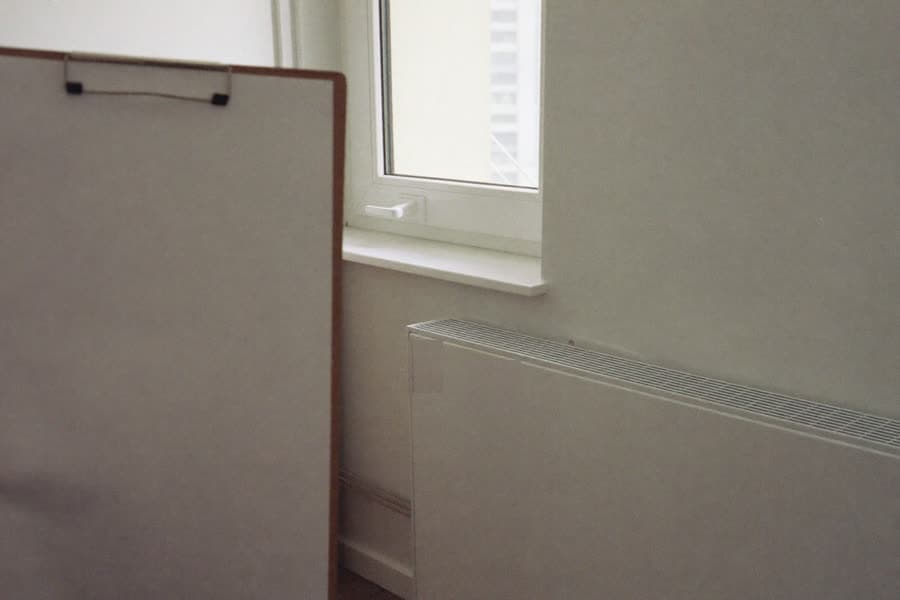 Ein leeres Klemmbrett wird in einer leergeräumten Wohnung vor Fenster und Heizkörper gehalten