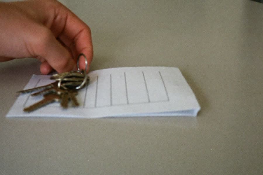 Eine Hand legt einen Schlüsselbund auf ein gefaltetes leeres Formular auf einem hellen Tresen